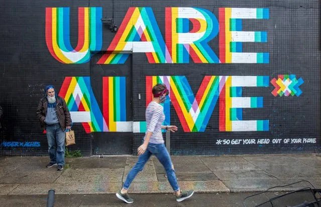 A pedestrian wearing a face mask or covering due to the COVID-19 pandemic, walks past a mural reading “U Are Alive..... so get your head out of your phone” in Dublin on October 19, 2020, amid reports that further lockdown restrictions could be imposed to help mitigate the spread of the novel coronavirus. Ireland will crank up coronavirus restrictions, prime minister Micheal Martin said last week, announcing a raft of new curbs along the border with the British province of Northern Ireland. (Photo by Paul Faith/AFP Photo)