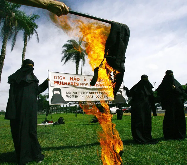 Brazilian women covered from head to toes burn a burka in support of Arabic women 10 May, 2005 in front of the Ulysses Guimaraes Convention Center in Brasilia. The demonstrators, who support the Arabic women's struggle for more freedom and social rights, are delivering a letter of protest to all the delegations attending the South American-Arab Summit in the Brazilian capital. (Photo by AFP Photo)
