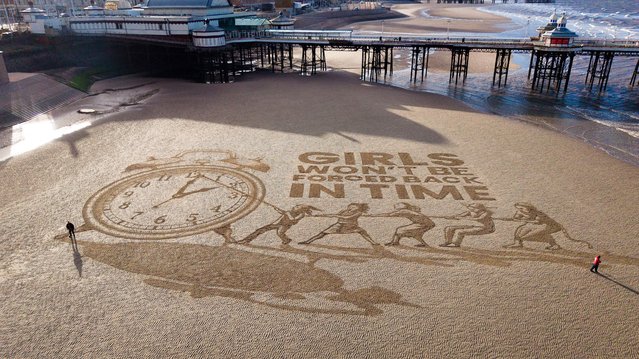 In this aerial view artists from Sand In Your Eye complete a drawing next to Blackpool's North Pier on the beach warning against “turning back the clock” on girls’ rights on October 23, 2025 in Blackpool, England. The artwork ahead of the clocks going back this weekend and was commissioned by global children’s charity Plan International UK. The sand drawing warns against ‘turning back the clock’ on girls’ rights, as new research reveals that one in three young Brits believe progress on gender equality is likely to reverse within their lifetime says the children's charity. (Photo by Christopher Furlong/Getty Images)