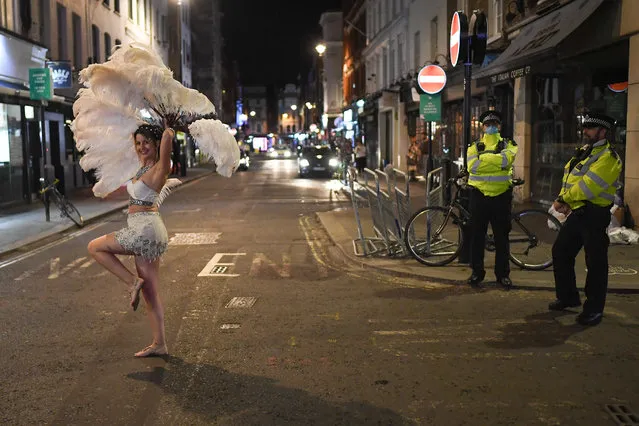 Police officers look on as an entertainer walks past in Soho on September 24, 2020 in London, England. Pubs, cafes and restaurants will have to shut at 10pm every night under new measures to control the rising rate of coronavirus. (Photo by Peter Summers/Getty Images)
