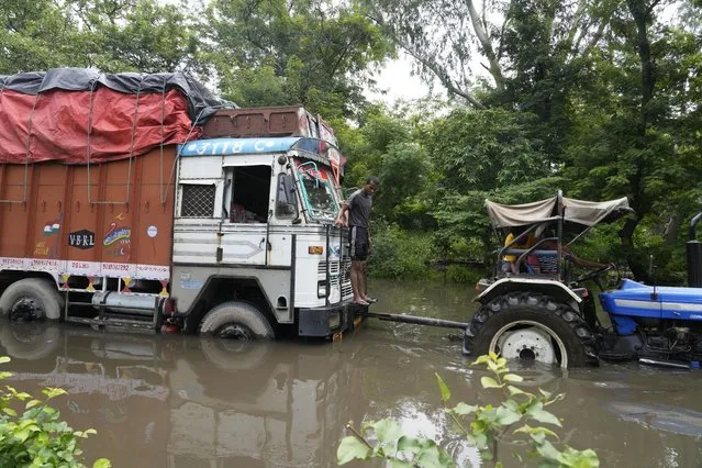 A truck stuck on a flooded street is pulled by a tractor following heavy rainfall in New Delhi, India, Thursday, July 13, 2023. (Photo by Manish Swarup/AP Photo)