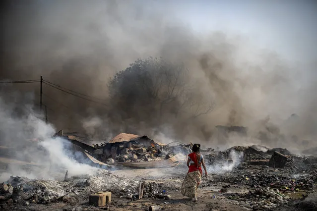 A woman walks barefoot near burning shanties at a slum area in Noida, a suburb of New Delhi, India, Sunday, April 11, 2021. Two children were killed and more than 150 huts of a slum inhabited mostly by ragpickers were gutted in a fire that broke out Sunday afternoon. (Photo by Altaf Qadri/AP Photo)