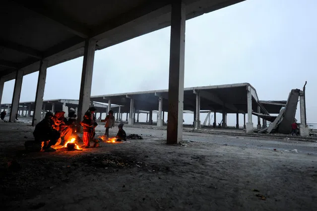 Syrians evacuated from eastern Aleppo keep warm by a fire, under a shelter in government controlled Jibreen area in Aleppo, Syria November 30, 2016. (Photo by Omar Sanadiki/Reuters)