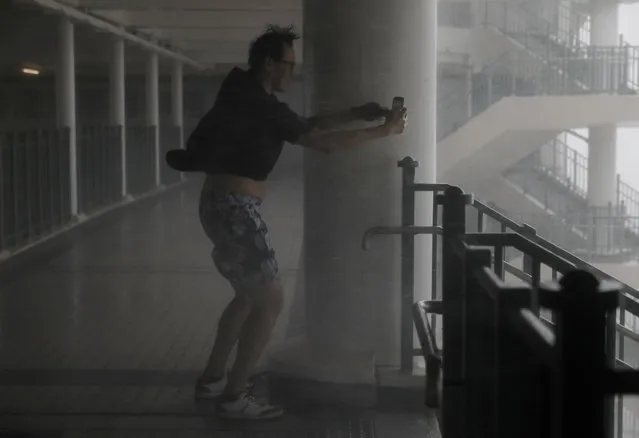 A man takes pictures against strong winds from Typhoon Mangkhut on the waterfront of Victoria Habour Hong Kong, Sunday, September 16, 2018. Hong Kong and southern China hunkered down as strong winds and heavy rain from Typhoon Mangkhut lash the densely populated coast. The biggest storm of the year left at least 28 dead from landslides and drownings as it sliced through the northern Philippines. (Photo by Vincent Yu/AP Photo)