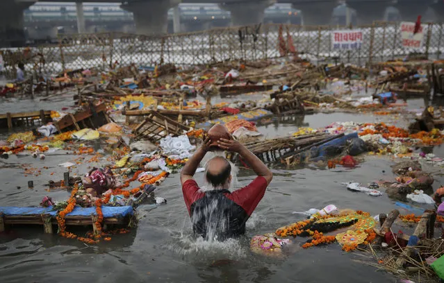In this October 19, 2018, photo,  an Indian Hindu devotee takes a ritualistic bath after immersing an idol of Hindu goddess Durga in the River Yamuna during Durga Puja festival in New Delhi, India. The immersion of idols marks the end of the festival that commemorates the slaying of a demon king by lion-riding, 10-armed goddess Durga, marking the triumph of good over evil. (Photo by Altaf Qadri/AP Photo)