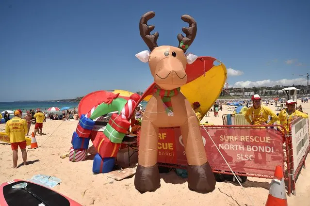 Surf lifesavers (L) walk past a Christmas tree and an inflatable reindeer on Bondi Beach on Christmas Day in Sydney on December 25, 2016. (Photo by Peter Parks/AFP Photo)