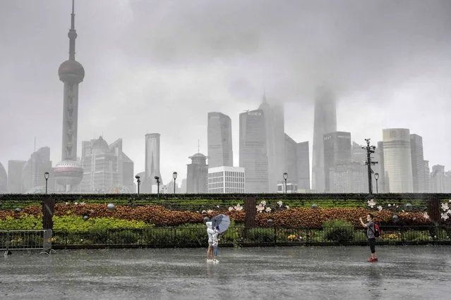 This photo taken on July 25, 2021 shows people posing for a photo along an empty Bund in Shanghai, as most people stay indoors due to wind and rain as Typhoon In-Fa lashes parts of the eastern Chinese coast. (Photo by Vivian Lin/AFP Photo)