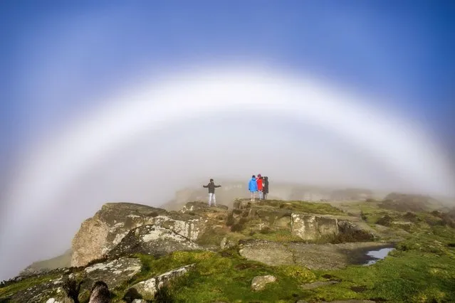 Walkers marvel at a fog bow over Curbar Edge, Derbyshire in the last decade of October 2023. The phenomenon is similar to a rainbow, but because the water droplets that cause fog are so small, its colours are very weak. (Photo by Richard Bowring/Animal News Agency)