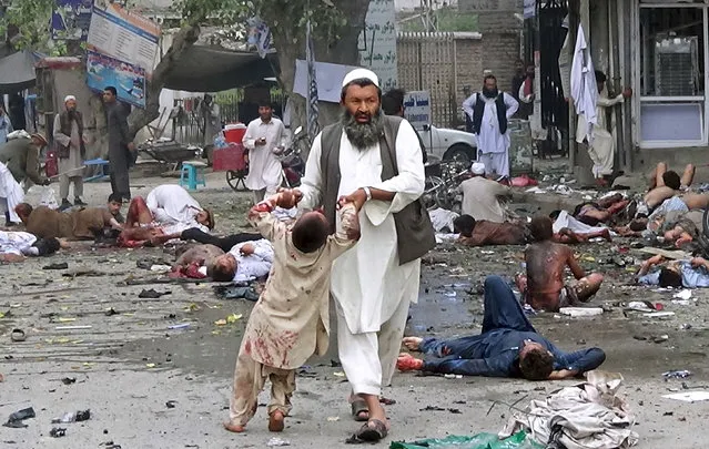 A man carries an injured boy after a suicide attack in Jalalabad April 18, 2015. The suicide bomb blast in Afghanistan's eastern city of Jalalabad killed 33 people and injured more than 100 outside a bank where government workers collect salaries, the city's police chief said on Saturday. (Photo by Reuters/Pajwak News Agency)