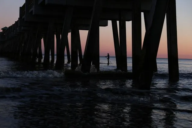 A man paddles board in silhouette under the Folly Beach Pier at sunset in Folly Beach, South Carolina on January 29, 2024. (Photo by Shannon Stapleton/Reuters)