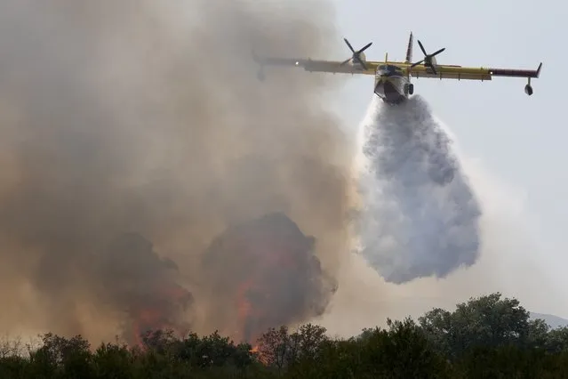 A firefighting airplane sprays a wildfire with water from nearby Adriatic sea, near Biograd, southern Croatia, Saturday, August 21, 2021. Several wildfires have been reported in the Adriatic region of Croatia. (Photo by Darko Bandic/AP Photo)