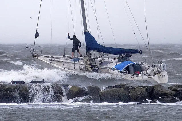 A boater stands on the bow of an anchored sailboat as waves crash over a breakwater in Alameda, Calif., Sunday, February 4, 2024, in Alameda, Calif. High winds and heavy rainfall are impacting the region. (Photo by Noah Berger/AP Photo)