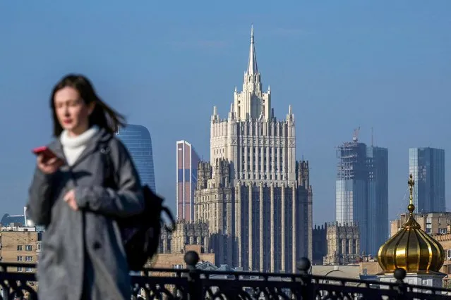 A woman looks at her phone as she walks across a bridge with the Russian Foreign Ministry building in the background, in central Moscow, on October 12, 2021. (Photo by Natalia Kolesnikova/AFP Photo)