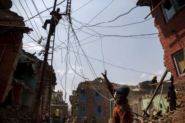 A local resident climbs on a utility pole as others clear the debris of their collapsed house after the earthquake at Harisiddhi village, on the outskirts of Kathmandu, Nepal, May 6, 2015. (Photo by Athit Perawongmetha/Reuters)