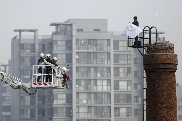 A man holds a handwritten petition atop a chimney as negotiators on an aerial ladder talk to him in Beijing April 8, 2014. The man was later convinced by negotiators to descend after spending three hours on the chimney, local media reported. (Photo by Reuters/Stringer)