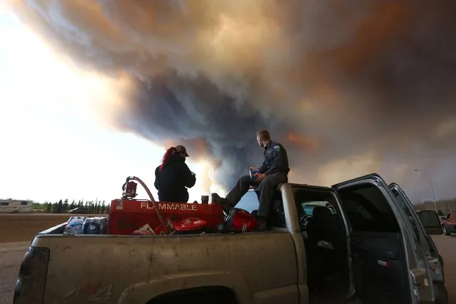 A group trying to rescue animals from Fort McMurray wait at  road block on Highway 63 as smoke rises from a forest fire near Fort McMurray, Alberta on May 6, 2016. 
Canadian police led convoys of cars through the burning ghost town of Fort McMurray Friday in a risky operation to get people to safety far to the south.In the latest chapter of the drama triggered by monster fires in Alberta's oil sands region, the convoys of 50 cars at a time are driving through the city at about 50-60 kilometers per hour (30-40 miles per hour) TV footage showed. (Photo by Cole Burston/AFP Photo)