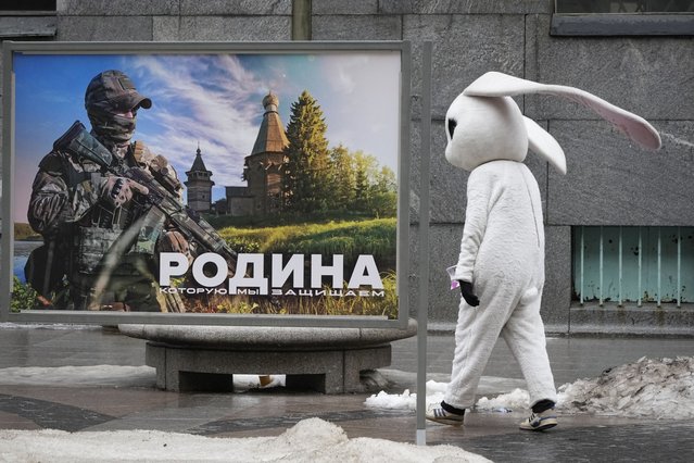 A street performer walks past an image of a Russian serviceman reading “The Motherland we defend” at a street exhibition of military photos in St. Petersburg, Russia, Tuesday, March 14, 2023. A campaign to replenish Russian troops in Ukraine with more soldiers appears to be underway again, with makeshift recruitment centers popping up in cities and towns, and state institutions posting ads promising cash bonuses and benefits to entice men to sign contracts enabling them to be sent into the battlefield. (Photo by AP Photo/Stringer)