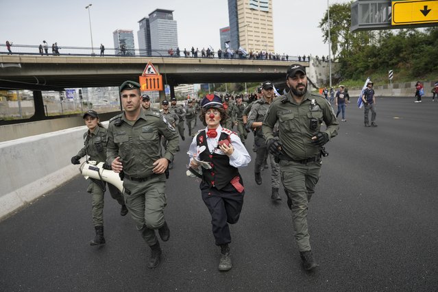 An Israeli activist dressed as a clown runs with border police as Israelis protest against plans by Prime Minister Benjamin Netanyahu's government to overhaul the judicial system block a free way in Tel Aviv, Israel, Thursday, March 23, 2023. (Photo by Oded Balilty/AP Photo)