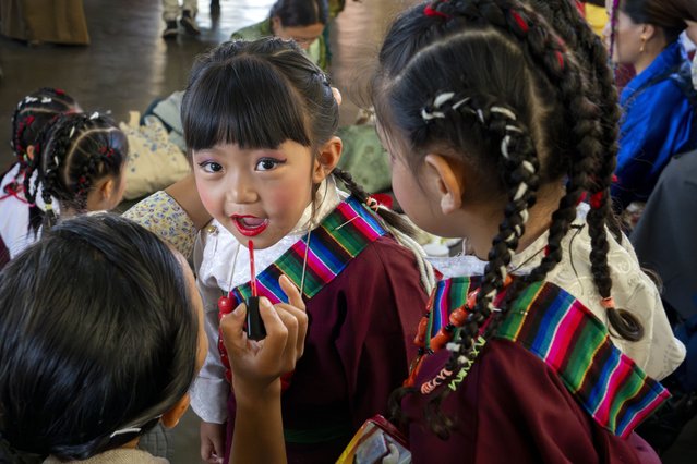 A young exiled Tibetan girl gets her lips painted by her teacher before she performs a traditional dance at an event to celebrate the 89th birthday of Tibetan spiritual leader the Dalai Lama at the Tsuglakhang temple in Dharamshala, India, Saturday, July 6, 2024. (Photo by Ashwini Bhatia/AP Photo)