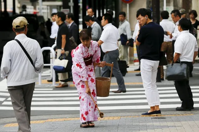 A woman wearing a kimono performs an uchimizu ritual outside a pachinko game parlor in Tokyo June 30, 2015. The splashing of water onto the hot asphalt in summer is an old Japanese tradition meant to cool down the air as the water evaporates. (Photo by Thomas Peter/Reuters)