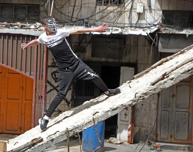 A Palestinian demonstrator hurls rocks amid clashes with Israeli security forces in Hebron city in the occupied West Bank, on April 1, 2022. Israeli forces shot dead a Palestinian man during clashes in the flashpoint occupied West Bank city of Hebron, the latest in a surge of violence, the Palestinian health ministry said. The Palestinian Wafa news agency identified the dead man as Ahmad al-Atrash, who had previously served six years in an Israeli prison. (Photo by Mosab Shawer/AFP Photo)