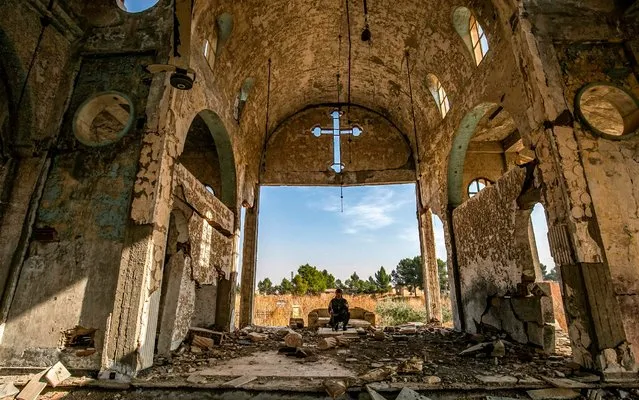 A member of the Khabour Guards (MNK) Assyrian Syrian militia, affiliated with the Syrian Democratic Forces (SDF), sits in the ruins of the Assyrian Church of the Virgin Mary, which was previously destroyed by Islamic State (IS) group fighters, in the village of Tal Nasri south of the town of Tal Tamr in Syria's northeastern Hasakah province on November 15, 2019. The few Assyrian Christians who escaped the Islamic State group invasion in 2015, and did not choose to emigrate, now anxiously watch the advance of Turkish forces toward their villages in southern Hassakeh province. (Photo by Delil Souleiman/AFP Photo)