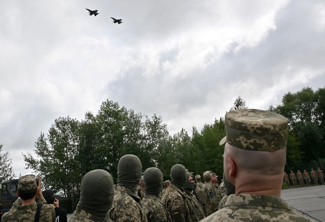 Ukrainian pilots and others look on as F16 fighter jets fly past during a ceremony held to mark Ukrainian Air Forces Day at undisclosed location on August 4, 2024. Ukraine has received its first batch of US-made F16 fighter jets, Ukrainian President Volodymyr Zelensky said Sunday, showing journalists several aircrafts that Kyiv hopes will help beat back Russian forces. (Photo by Sergei Supinsky/AFP Photo)