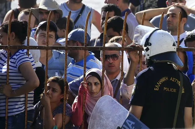 A Greek riot police officer (front R) stands guard as migrants and refugees wait a registration procedure at the national stadium of the Greek island of Kos, August 12, 2015. Greek police used fire extinguishers and batons against migrants on the island of Kos on Tuesday after violence broke out in a sports stadium where hundreds of people, including young children, were waiting for immigration papers. (Photo by Alkis Konstantinidis/Reuters)