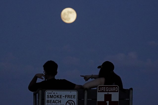 People watch the rising moon Monday, June 13, 2022, in East Boston, Mass. The moon will reach its full stage on Tuesday, during a phenomenon known as a supermoon because its proximity to Earth, and it is also labeled as the “Strawberry Moon” because it is the full moon at strawberry harvest time. (Photo by Charlie Riedel/AP Photo)