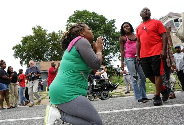 A woman prays in the street as police advance on Page Ave. to try to disperse a crowd that gathered after a shooting incident in St. Louis, Missouri August 19, 2015. (Photo by Lawrence Bryant/Reuters)