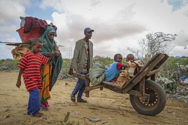 A local resident uses a wheelbarrow to transport the young children of a woman who fled drought-stricken areas as she arrives at a makeshift camp for the displaced on the outskirts of Mogadishu, Somalia Thursday, June 30, 202. (Photo by Farah Abdi Warsameh/AP Photo)