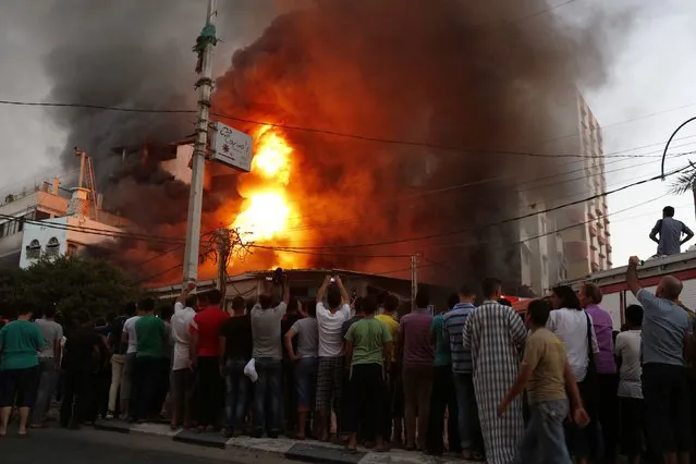 People watch as a fire burns in a building that witnesses say was hit by an Israeli air strike in Gaza City August 10, 2014. Israel has accepted a new Gaza ceasefire proposed by Egyptian mediators and will send negotiators to Cairo on Monday if the truce holds, Israeli officials said. (Photo by Siegfried Modola/Reuters)