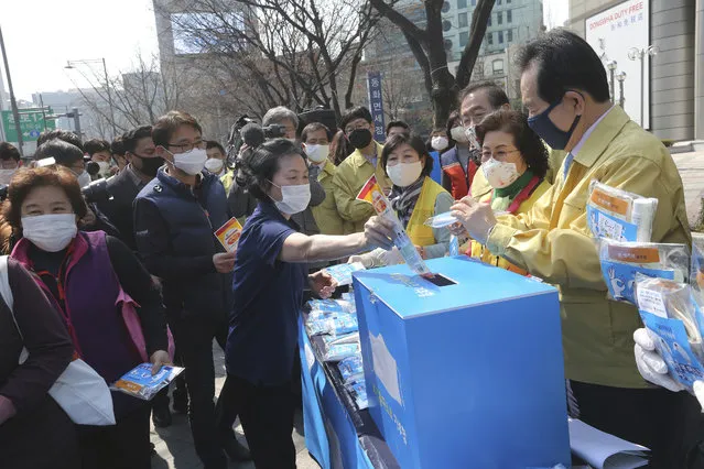 A woman puts an envelope containing a face mask into a charity box as South Korean Prime Minister Chung Se-kyun, right, watches during a campaign for the donation of face masks to impoverished people amid the spread of the new coronavirus in Seoul, South Korea, Wednesday, March 25, 2020. (Photo by Ahn Young-joon/AP Photo)