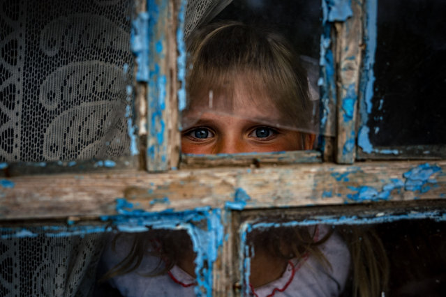 Antonina, 9, looks through a shrapnel-broken window after an online lesson on the first school day at her home in the village of Pokrovske, on September 1, 2022, amid Russian invasion of Ukraine. In Pokrovske, a tiny village of 24 people in the Mykolayev region of southern Ukraine, nine-year-old Antonina Sidorenko started school to the steady sound of cannons in this town near the front line. (Photo by Dimitar Dilkoff/AFP Photo)