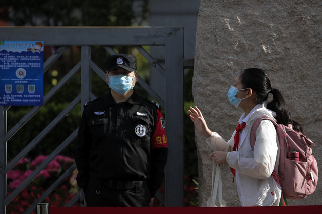 A student wearing a protective face mask to help curb the spread of the new coronavirus waves to teachers as she arrives for the reopening of a primary school in Beijing, Monday, June 1, 2020. With declining virus case numbers, students have gradually returning to their classes in the capital city. (Photo by Andy Wong/AP Photo)