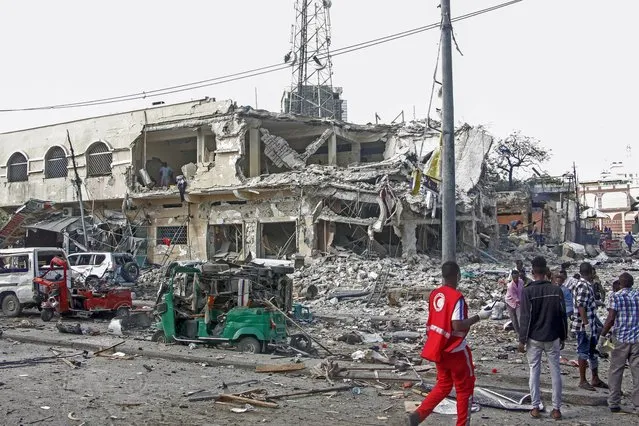 People observe a destroyed building and vehicles at the scene of a two car bombs attack in Mogadishu, Somalia, Saturday October 29, 2022. (Photo by Farah Abdi Warsameh/AP Photo)