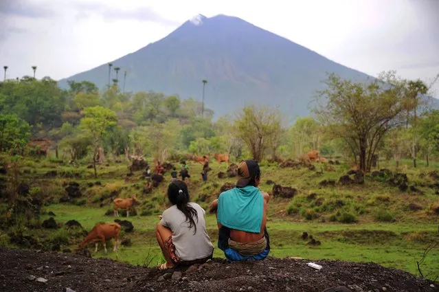 Villagers look at the Mount Agung volcano from Kubu sub-district in Karangasem Regency on Indonesia's resort island of Bali on December 3, 2017. Tens of thousands have already fled their homes around the volcano – which last erupted in 1963, killing around 1,600 people – but as many as 100,000 will likely be forced to leave in case of a full eruption, disaster agency officials have said. (Photo by Sonny Tumbelaka/AFP Photo)