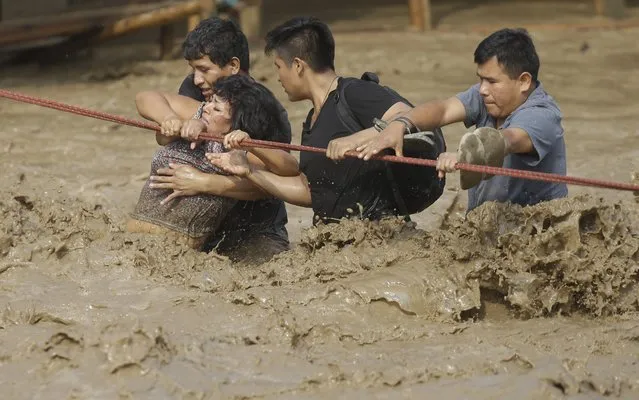 People stranded in floodwaters hold onto a rope as they wade to safety in Lima, Peru, on March 17, 2017. Intense rains and mudslides wrought havoc around the Andean nation and caught residents in Lima, a desert city of 10 million where it almost never rains, by surprise. (Photo by Martin Mejia/AP Photo)