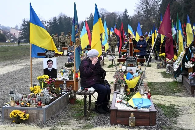An elderly woman grieves next to the grave of a Ukrainian soldier during Ukraine's Army Day at Lychakiv Cemetery in the western Ukrainian city of Lviv on December 6, 2022, amid the Russian invasion of Ukraine. (Photo by Yuriy Dyachyshyn/AFP Photo)