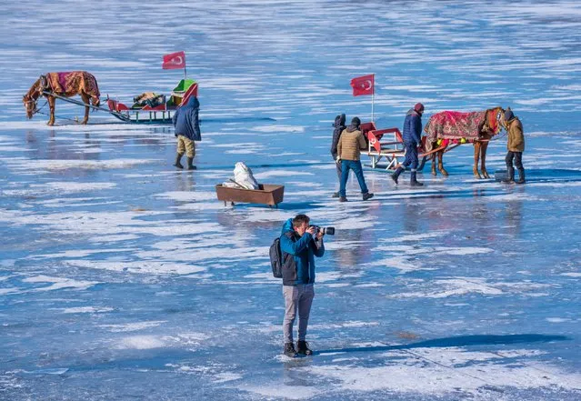 A man takes photos of horse-drawn sleighs on the frozen surface of Lake Cildir in Kars, Turkiye on December 29, 2022. Visitors take the opportunity to walk and get on horse-drawn sleigh on the frozen surface of the lake. (Photo by Ismail Kaplan/Anadolu Agency via Getty Images)