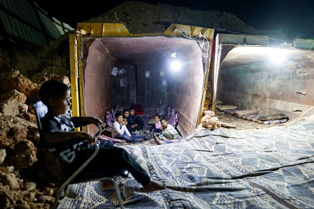 Children sit inside a makeshift tunnel made from a truck cargo trailer buried under dirt, where they hide when a rocket siren alert sounds for a missile strike from Iran on Israel, in southern Negev, Israel on June 18, 2025. (Photo by Amir Cohen/Reuters)