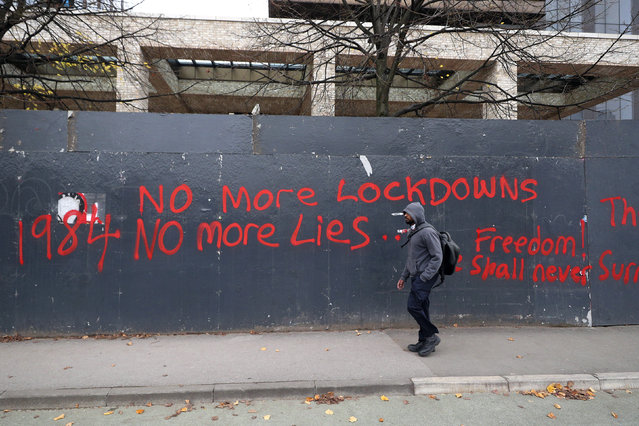 A man walks past anti-lockdown graffiti in Manchester, England, Monday, October 19, 2020 as the row over Greater Manchester region's coronavirus status continues. Britain’s government says discussions about implementing stricter restrictions in Greater Manchester must be completed Monday because the public health threat caused by rising COVID-19 infections is serious and getting worse. (Photo by Peter Byrne/PA Wire via AP Photo)