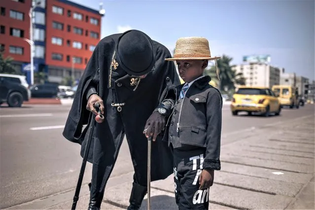 A performer and his son parade during a gathering of sapeurs in Kinshasa, capital of the Democratic Republic of Congo, on February 10, 2023. Flamboyant dandies paraded near the tomb of one of their icons in DR Congo's capital Kinshasa, flaunting coveted designer labels in stark contrast to the grinding poverty surrounding them. Dozens of extravagantly dressed dandies, known locally as sapeurs, turned up on February 10, 2023 to commemorate the death of Stervos Niarcos, a pop star and one of the most famous of Congo's legendary dandies. Niarcos, who died in 1995, epitomises the fanatical pursuit of elegance for many in the abysmally poor central African country.  (Photo by Alexis Huguet/AFP Photo)