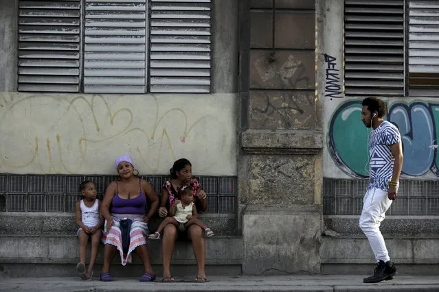 A man walks past two women as they sit with their daughters on a sidewalk in Havana October 26, 2015. (Photo by Enrique De La Osa/Reuters)