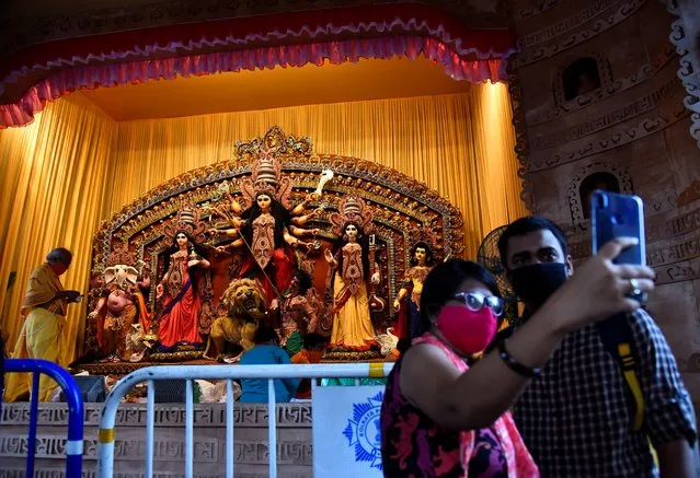 Hindu devotees take a selfie in front of an idol of Hindu goddess Durga before prayer at a cordoned off “pandal” or temporary platform, on the first day of Durga Puja festival, amidst the spread of COVID-19 in Kolkata, India, October 22, 2020. (Photo by Ranita Roy/Reuters)