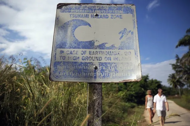 Tourists walk behind a faded sign warning of tsunami hazard in Khao Lak, Phang Nga province December 15, 2014. Ahead of the anniversary of the 2004 tsunami, experts and officials say key weaknesses remain across the region in the system designed to warn people of the next disaster, and get them to safety. (Photo by Damir Sagolj/Reuters)