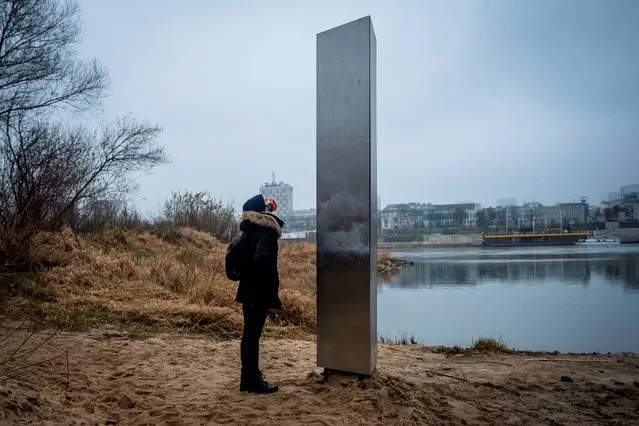 A woman looks on December 10, 2020 at a metal monolith that has popped up on a riverbank of the Vistula in the Polish capital Warsaw, the latest in a string of similar objects that have recently appeared in Europe and the US. Similar-looking objects were found in the United States, Romania and Britain. (Photo by Wojtek Radwanski/AFP Photo)