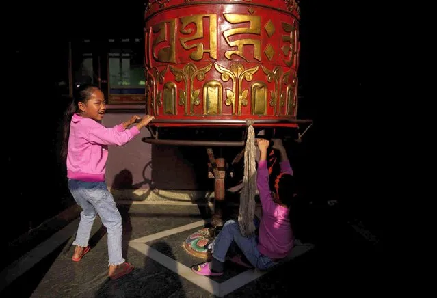 Young girls play on a prayer wheel during the Temal festival at Boudhanath Stupa in Kathmandu, Nepal, Wednesday, April 5, 2023. During this festival people from the Tamang community gather in nearby monasteries or stupas light butter lamp performs rituals to pay homage to their loved ones who have passed away. (Photo by Niranjan Shrestha/AP Photo)