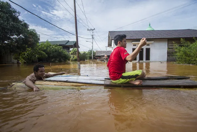 People use a makeshift raft to cross through a flooded village in Banjar, South Kalimantan on Borneo Island, Indonesia, in this Saturday, January 16, 2021 photo. Many thousands of people have been evacuated and a number have been killed in recent days in flooding on Indonesia's Borneo island, officials said Sunday. (Photo by Putra/AP Photo)