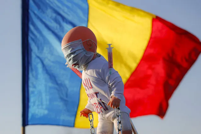 Anti-vaccination protesters hold a doll with “I don't want to be a lab rat” written on it backdropped by a Romanian national flag, during a rally outside the parliament building in Bucharest, Romania, Sunday, March 7, 2021. Some thousands of anti-vaccination protestors from across Romania converged outside the parliament building protesting against government pandemic control measures as authorities announced new restrictions amid a rise of COVID-19 infections. (Photo by Vadim Ghirda/AP Photo)